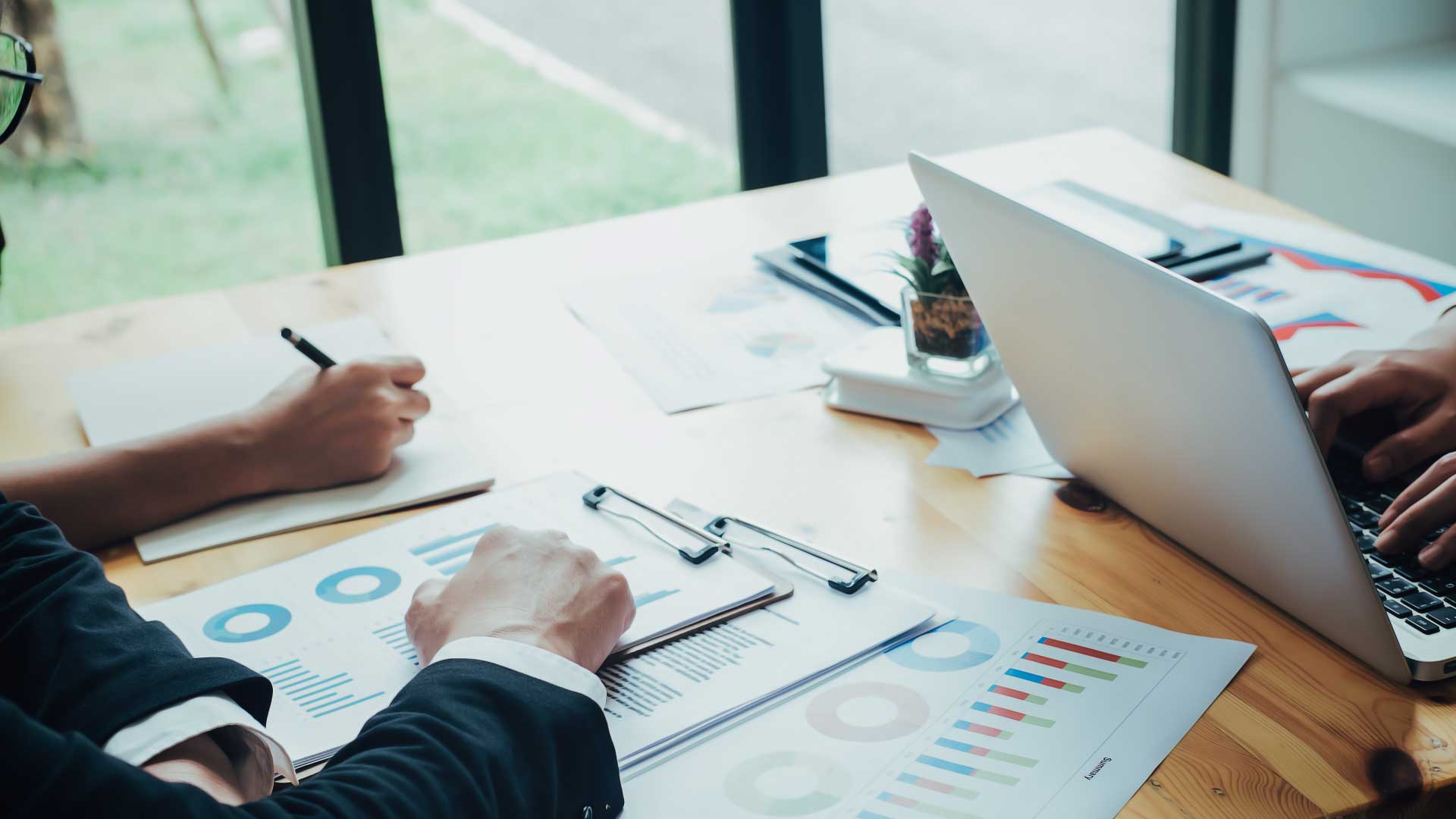 Business professionals reviewing jet cost reports and financial dashboards on a wooden desk with a laptop and printed charts, representing private jet cost transparency and real-time bookkeeping.