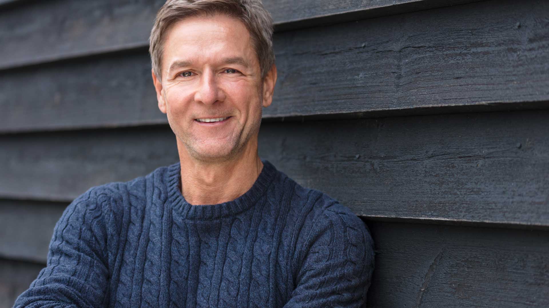 Smiling man standing against a modern wood-panel wall, representing La Casa Jet’s expert guidance for first-time private jet buyers.