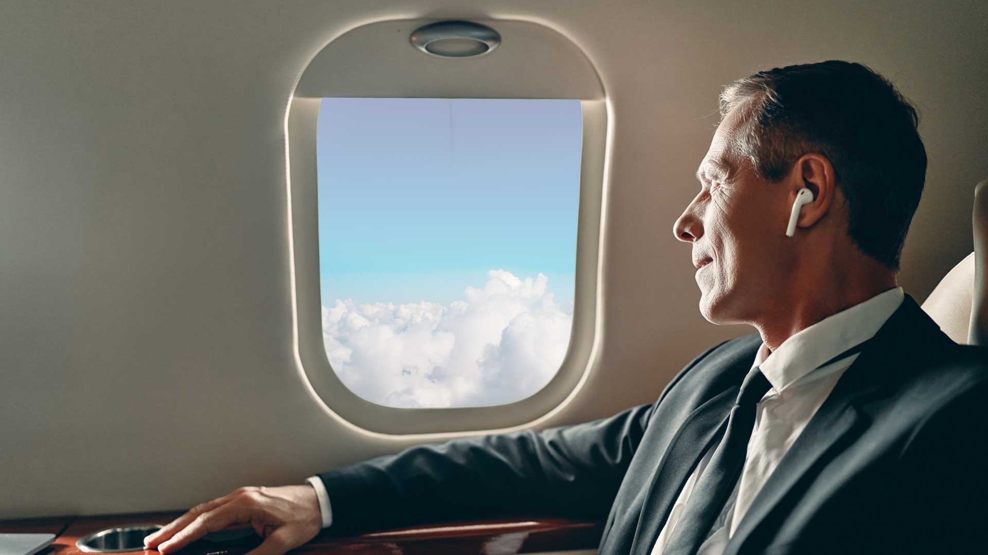 Businessman seated in a private jet looking out the window at clouds, representing La Casa Jet’s seamless aircraft ownership services.