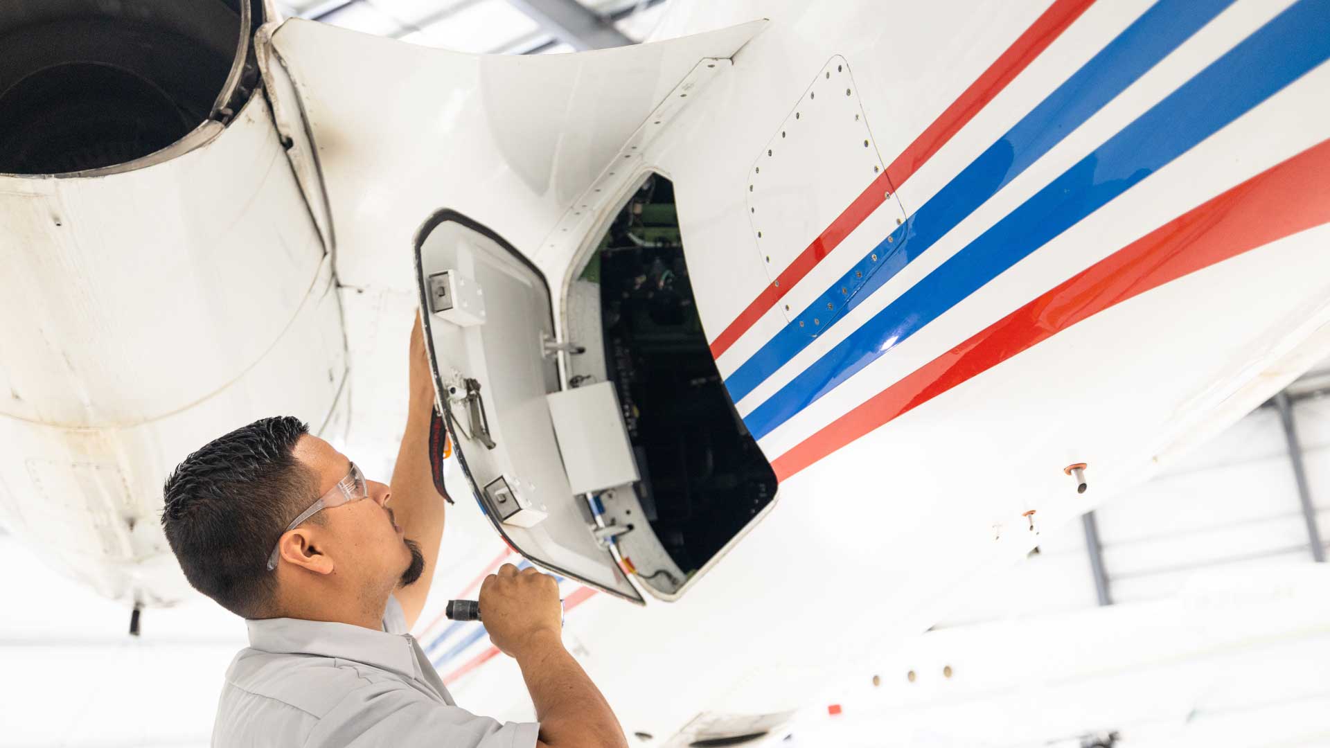Aircraft maintenance technician inspecting a jet engine compartment inside a brightly lit hangar, representing La Casa Jet’s real-time maintenance tracking and oversight services.